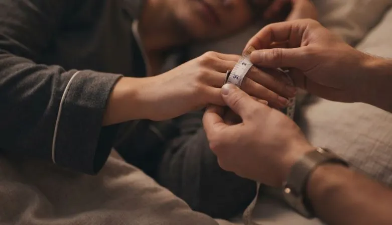 A man secretly measuring ring size of his partner while she is sleeping